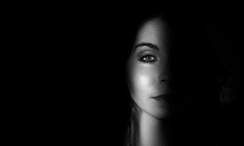 Black and white photo of woman in shadow with a beam of light illuminating part of her face.
